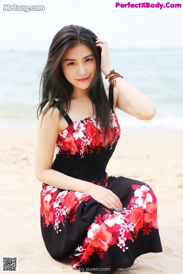A woman in a red and black dress sitting on the beach.