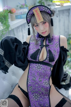 A woman in a black and purple lingerie posing on a white couch.