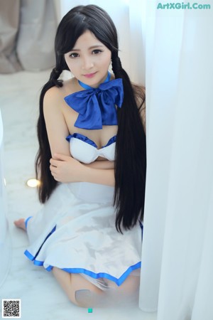 A woman in a white and blue dress sitting on a bed.