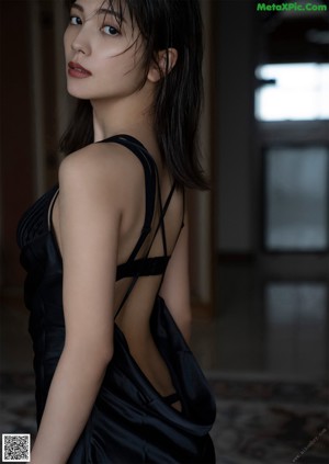 A woman in a black dress sitting on a bed.