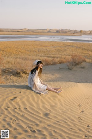 A woman sitting on top of a sandy beach.