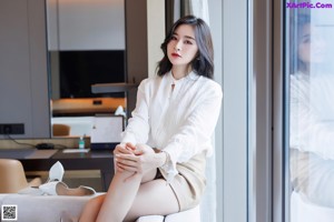 A woman sitting on top of a couch next to a window.