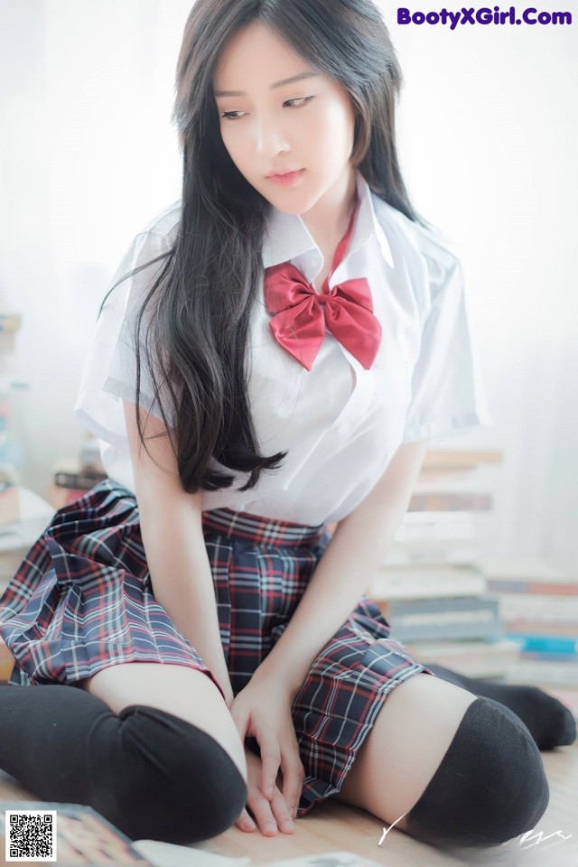 A woman in a school uniform sitting on the floor.