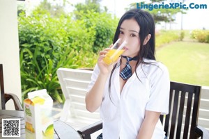 A woman in a school uniform drinking a glass of orange juice.